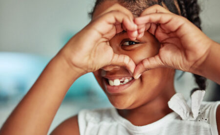 smiling young girl making a heart shape with her hands and looking through it